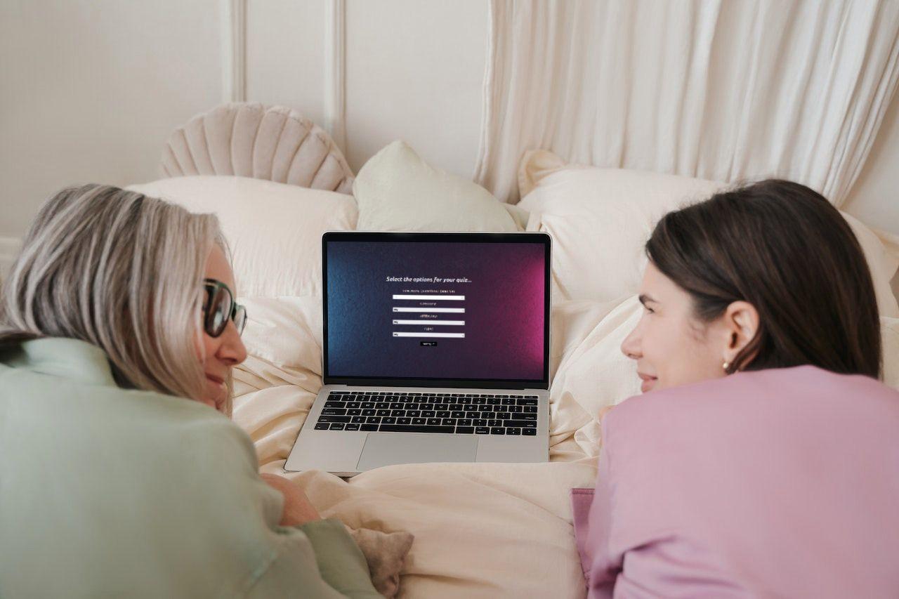 two people laying on a bed playing the quiz app on a laptop