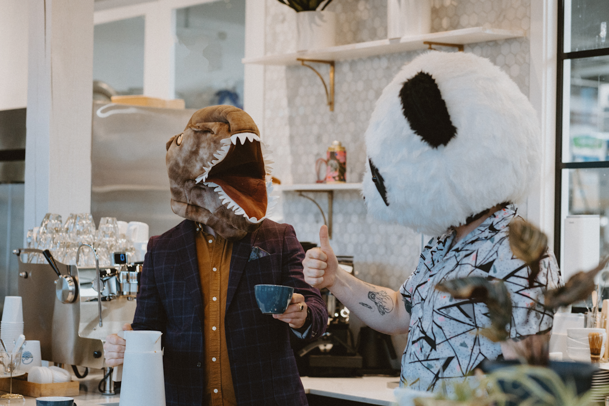 two people in a cafe one dressed as a dino the other as a panada giving the thumbs up